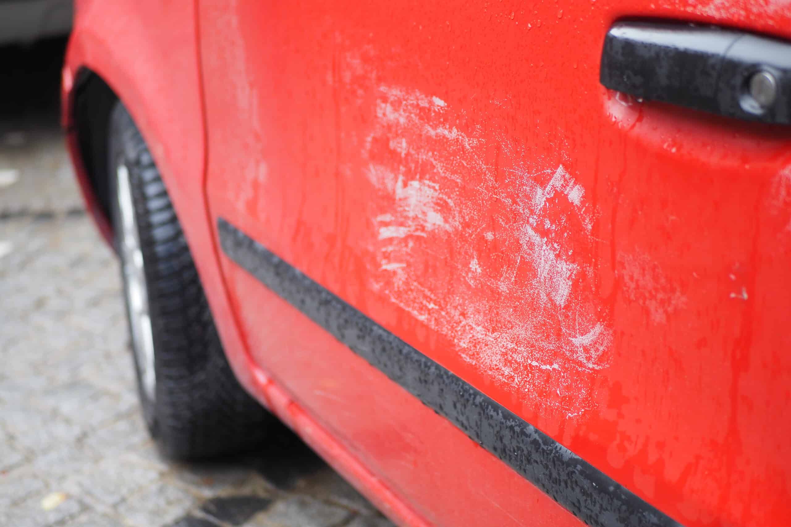 Scratches and scuff marks on a red car panel before paint restoration